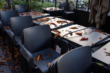 Closed outdoor café seating covered in autumn leaves