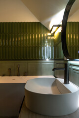 Basin and black faucet in green bathroom with lighting. Cozy spa nook.