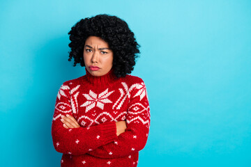 Upset woman in a red festive sweater standing against a bright blue background showing folded arms...