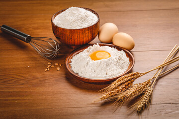 Fresh flour with eggs and wheat stalks on wooden table - baking ingredients for homemade bread and pastry making