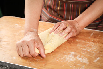 Woman kneading fresh wheat dough on floured wooden board for homemade baking