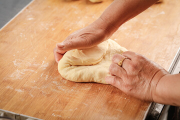 Hands kneading fresh wheat dough with flour on wooden board - traditional bread making