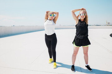 Fototapeta premium Two athletic women stretch arms overhead on sunny rooftop