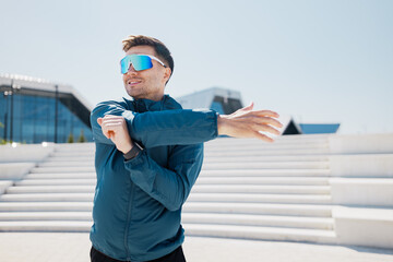 Man warming up arm muscles before run near a modern building
