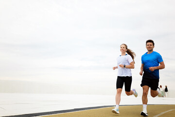 Fototapeta premium Couple running together on a track in athletic apparel near the ocean