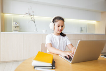 Girl learning on laptop at home in the kitchen with headphones