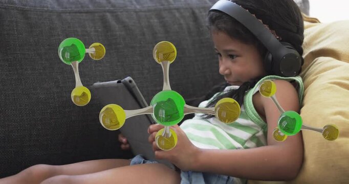 Girl tapping tablet on sofa and viewing green-gold molecular models drifting for education