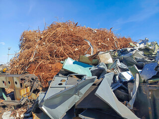 Large pile of rusty and shiny metal waste in a scrap yard under blue sky, symbolizing recycling,...
