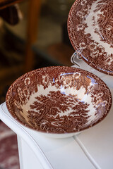 Two vintage British plates with brown landscape pattern on white wooden table. 