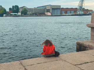 lonely girl sits on the riverbank in the city