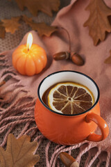 Orange mug of tea surrounded by autumn leaves, acorns and pumpkin-shaped candle creating warm seasonal atmosphere