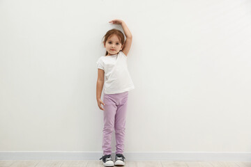 Cute little girl measuring her height near white wall