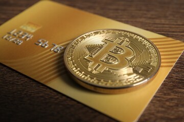 Bitcoin and plastic bank card on wooden table, closeup