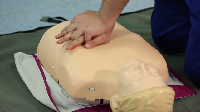 A close-up shows hands performing chest compressions on a CPR training dummy, demonstrating life-saving techniques during a first aid course.