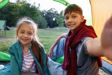 Happy brother and sister taking selfie in camping tent outdoors