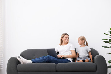 Mother and daughter spending time together on sofa at home. Space for text