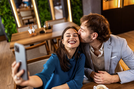 Smiling young couple in modern cafe taking selfie with smartphone, casual lifestyle moment. - Powered by Adobe