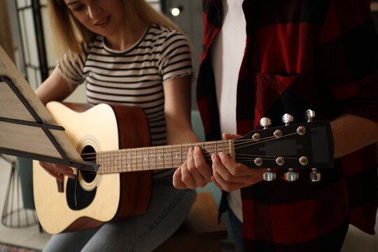 Tutor teaching woman to play guitar at home, closeup