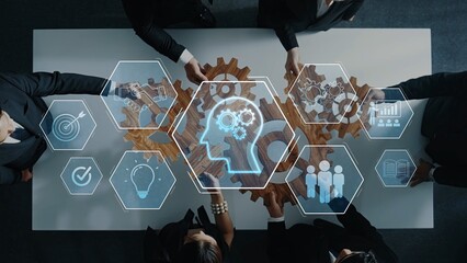 A group of business professionals engages in a collaborative session around a table, using gears and digital icons to symbolize innovative problem-solving and strategic planning. Raster