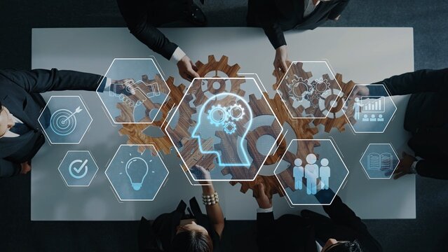 A group of business professionals engages in a collaborative session around a table, using gears and digital icons to symbolize innovative problem-solving and strategic planning. Raster