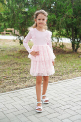 Fototapeta premium A confident young girl stands in a light pink frilly dress with her hand on her hip in a park setting