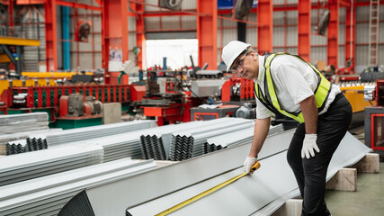 Industrial workers in safety helmets and vests measuring metal sheets inside a modern factory,...
