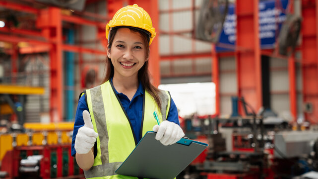 Smiling female engineer wearing safety helmet and vest holding clipboard in modern factory, representing industry, engineering, teamwork, occupational safety, and professional success. - Powered by Adobe