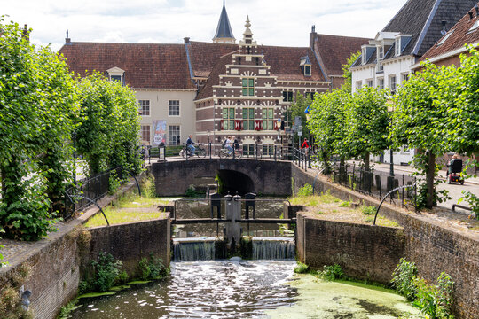 A picturesque scene in the city of Amersfoort captures a scenic canal flanked by rows of lush green trees. In the background, a historic building with intricate architecture stands proudly.