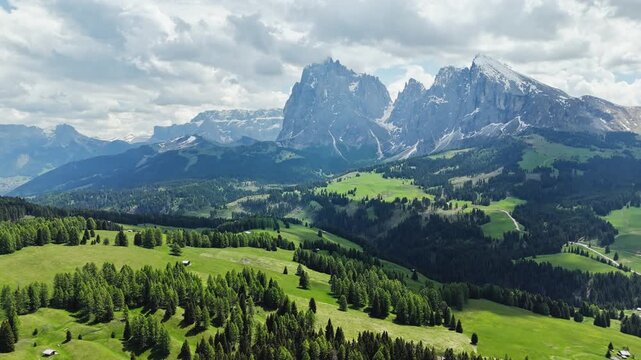 Forest patches and open grasslands under cloud shadows, Langkofel skyline, aerial view. Dolomite highlands with summer vegetation