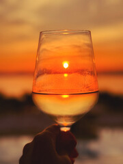 The setting sun reflects in a glass of white wine