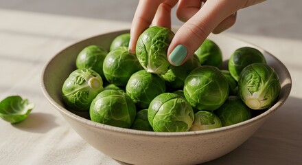 Hand Picking Fresh Brussels Sprouts from Ceramic Bowl with Natural Sunlight on Table