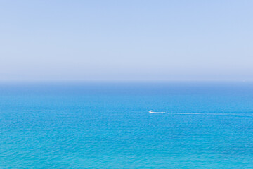 Obraz premium Serene expanse of blue ocean with a motorboat is wake in the foreground and a distant sailboat, perfect for travel, lifestyle, or maritime branding.