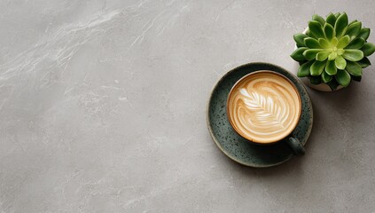 Atop a gray stone surface, a muted green mug holds latte art. A small succulent plant sits beside it