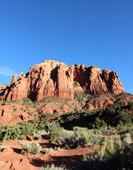 Fototapeta premium Red rock mesa against a vibrant blue sky. Desert landscape with scrub brush and rocky terrain leading up to a prominent mesa