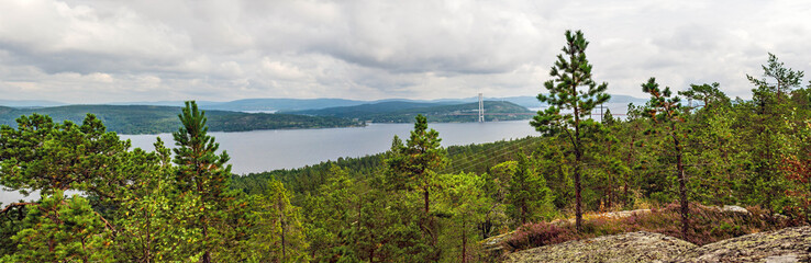 Naklejka premium Panoramic view of the Angermanalven river and the High Coast Bridge from a forested hill, showcasing the natural beauty and engineering marvel of Sweden's High Coast