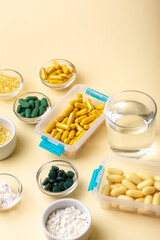 Vitamins, minerals and dietary supplements in containers and glass bowls, glass of water from above on yellow background. Assortments of many colored pills, tablets, capsules and food supplements. 