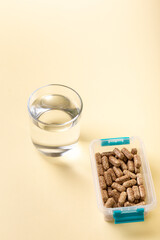 Vitamins, minerals and dietary supplements in containers and glass bowls, glass of water from above on yellow background. Many pills, tablets, capsules and food supplements. Healthy lifestyle