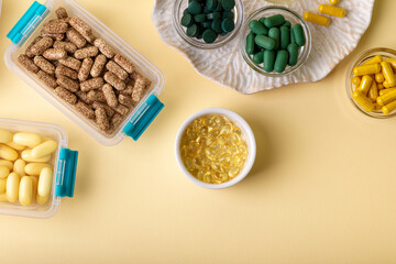 Vitamins, minerals and dietary supplements in containers and glass bowls from above on yellow background. Assortments of many colored pills, tablets, capsules and food supplements. Healthy lifestyle.