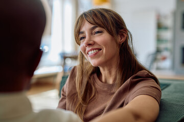 Happy woman smiling and engaging in conversation with a man while relaxing together on a cozy sofa in their inviting living room