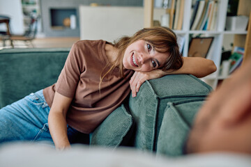 Happy young woman lying on a cozy green sofa, smiling and enjoying her free time, embracing...