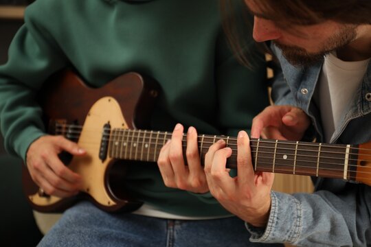 Tutor teaching man to play guitar at home, closeup