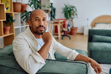 Fototapeta premium Relaxed African American man sitting comfortably on a sofa in a modern apartment, enjoying a moment of peace and tranquility indoors