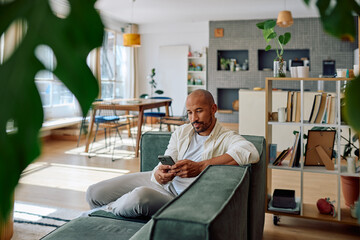 Young man using mobile phone while relaxing on comfortable sofa in his modern and bright apartment © we.bond.creations