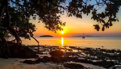 Rocky shoreline during a vivid sunset, framed by tree branches with leaves