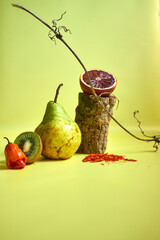 Creative still life with fresh pear, kiwi, chili pepper and blood orange on a vibrant yellow background. Minimalist food composition, modern art concept for healthy lifestyle and design projects