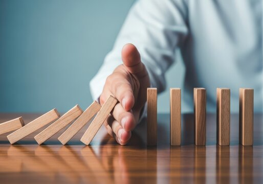 A persons hand stopping a line of falling dominoes, symbolizing risk management and crisis intervention