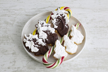 Cookies shaped like pine cones and Christmas trees, coated with chocolate and white icing, arranged on a festive display.