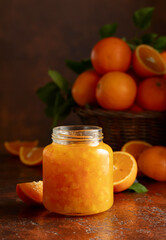 Orange jam and fresh fruits on a brown table.