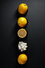 Fresh, juicy lemons and sugar cubes in small black bowls on a black background.