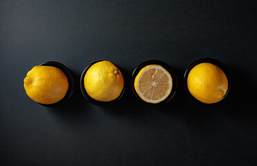 Fresh, juicy lemons in small black bowls on a black background.